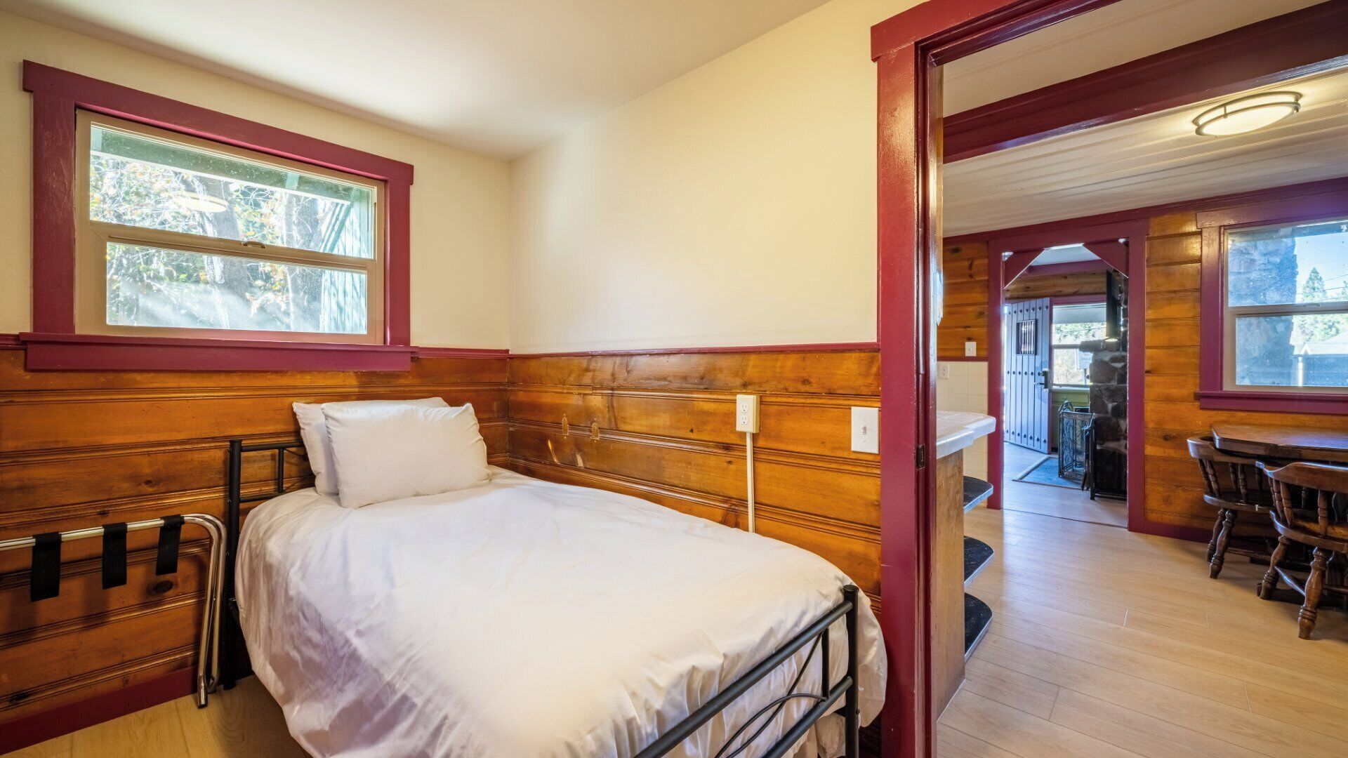 A single bed in a room with wooden paneling, a window, and a view of a dining area.