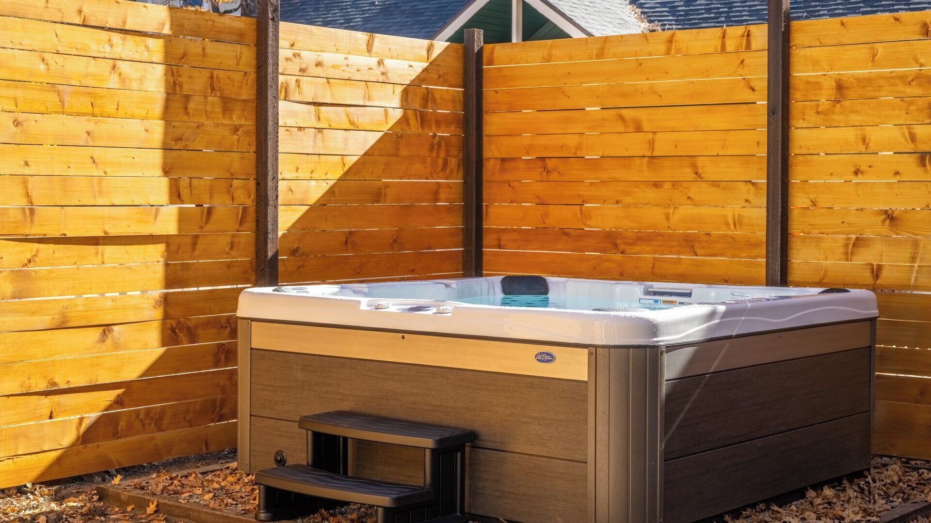 A hot tub with a wooden deck and a metal frame, surrounded by a wooden fence.