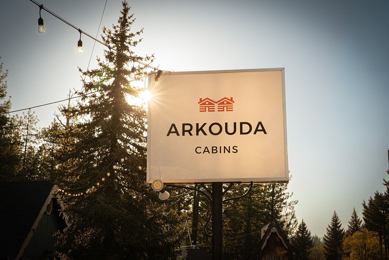 A sign for Arkouda Cabins with a logo of a house and trees.