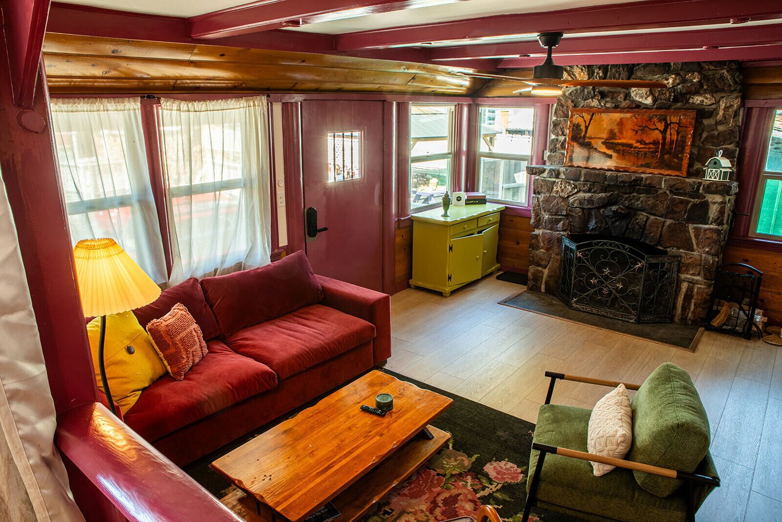 A cozy room with a red sofa, a wooden coffee table, a green armchair, a stone fireplace, and a yellow cabinet.