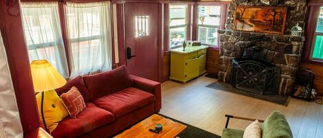 A cozy room with a red sofa, a wooden coffee table, a green armchair, a stone fireplace, and a yellow cabinet.