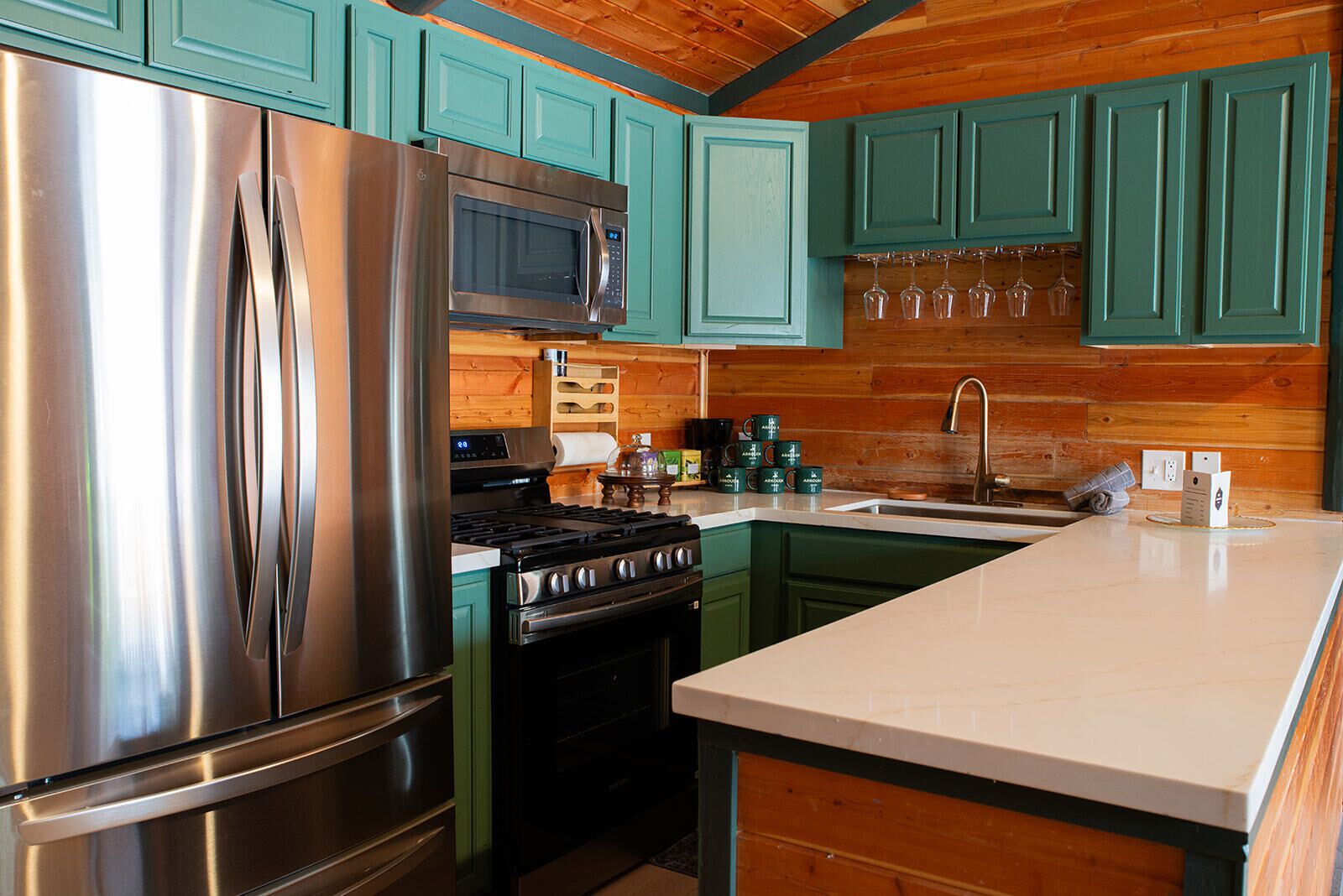 A kitchen with stainless steel appliances, teal cabinets, and a wooden ceiling.