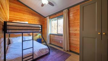 A bunk bed room with a ceiling fan, a window with curtains, and a door.