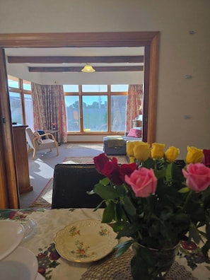 A room with a dining table set for a meal, a sofa, and a view through a large window.
