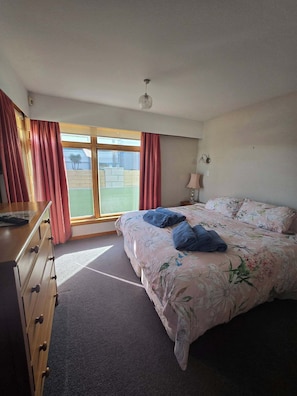 Une chambre à coucher avec un lit, une commode, une lampe et une vue sur l’extérieur.
