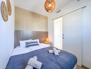 Une chambre d’hôtel avec un lit, une table de chevet avec une lampe, une porte et un mur orné d’un motif texturé.