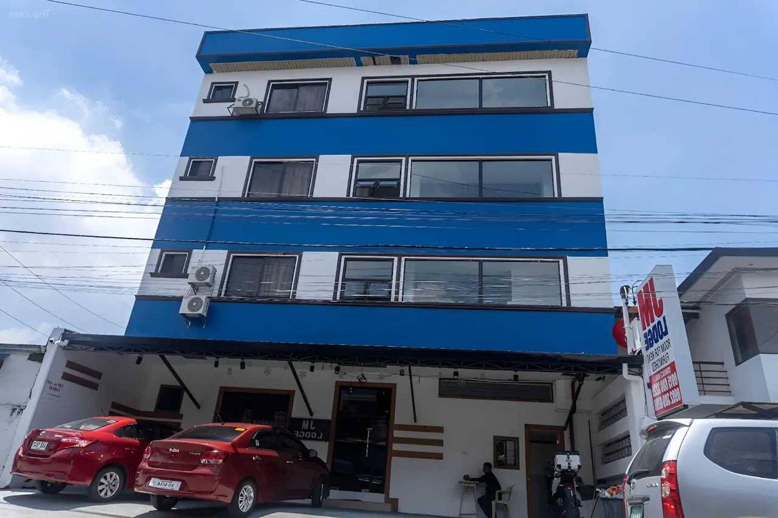 A multi-story building with a blue and white facade, featuring a ground-level entrance with a signboard.