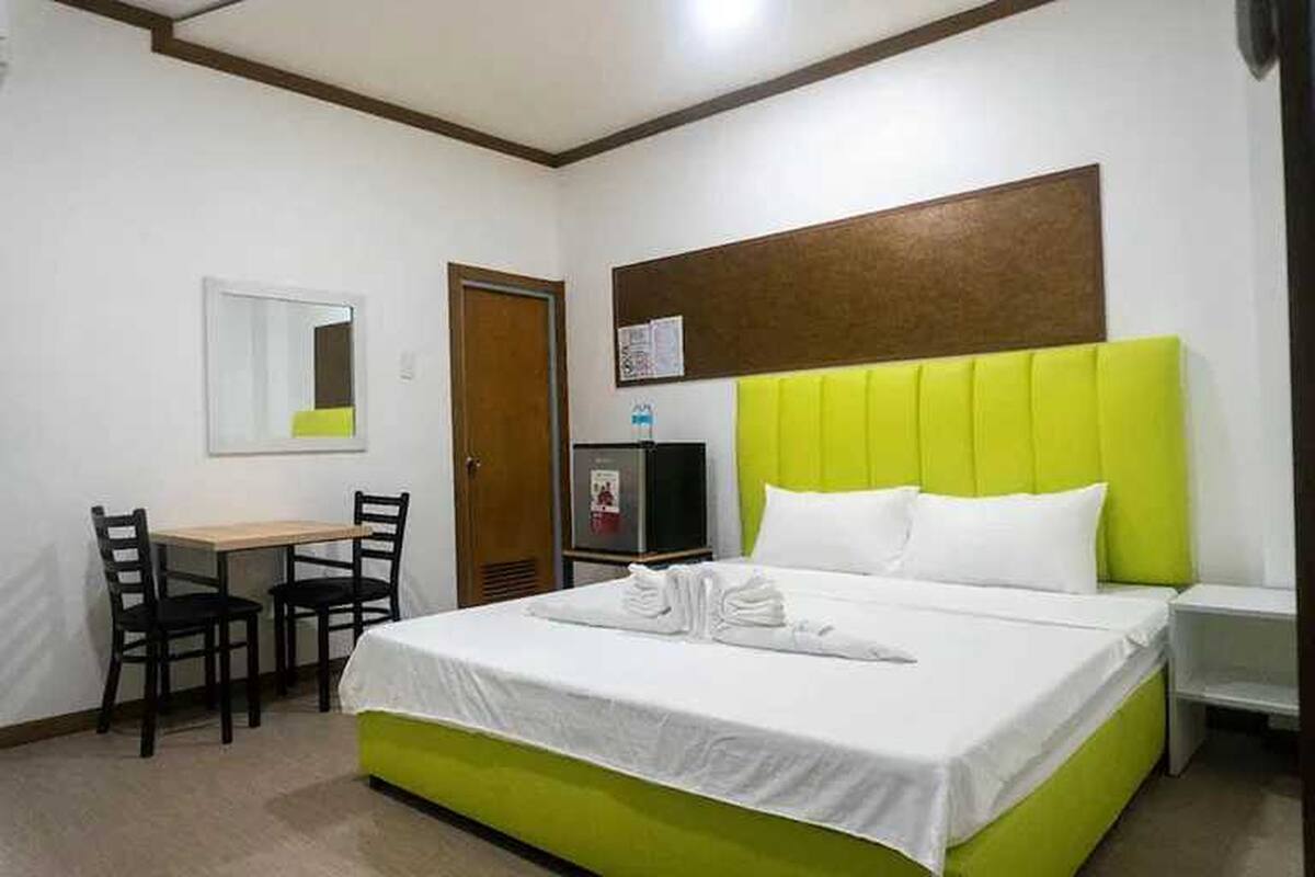 Een hotelkamer met een bed, een bureau, twee stoelen, een televisie en een spiegel.