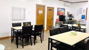 Un comedor con mesas y sillas, una máquina de café y un refrigerador.