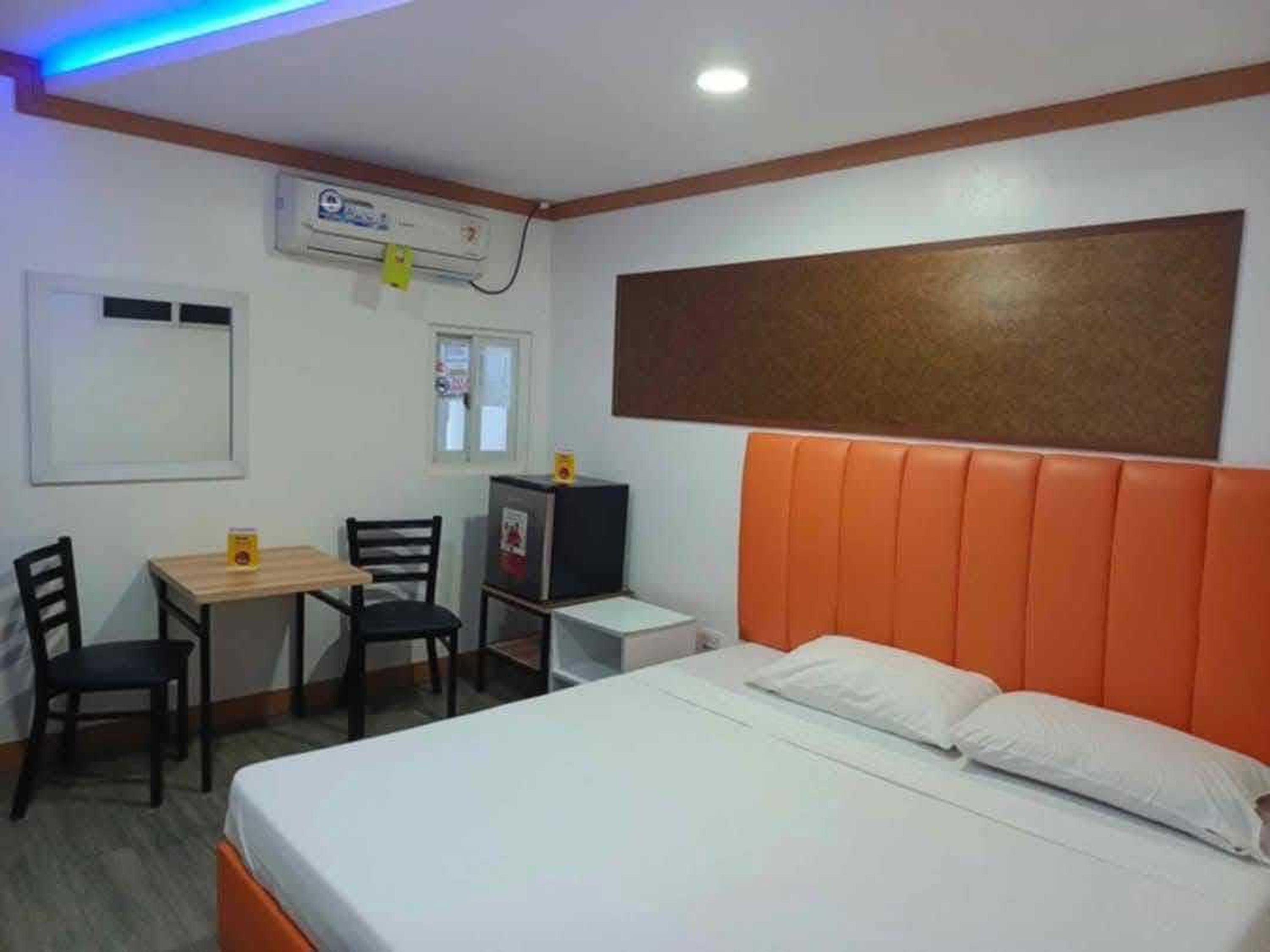 A hotel room with a bed, a desk, two chairs, a small table, and a refrigerator.