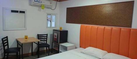 A hotel room with a bed, a desk, two chairs, a small table, and a refrigerator.