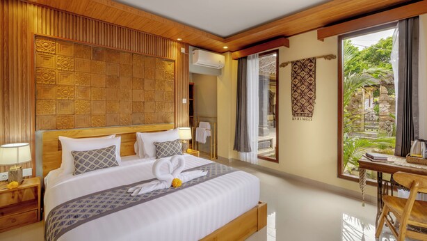 A hotel room with a large bed, wooden headboard, and a view of a garden through a sliding door. - Poset Unique Inn (Ubud)