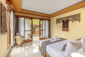 A hotel room with a bed, a desk, and a chair. There is a view of the outside through a glass door. - Poset Unique Inn (Ubud)