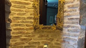 Un baño con pared de piedra, un lavabo redondo, un espejo con marco dorado y una toalla colgada en la pared.