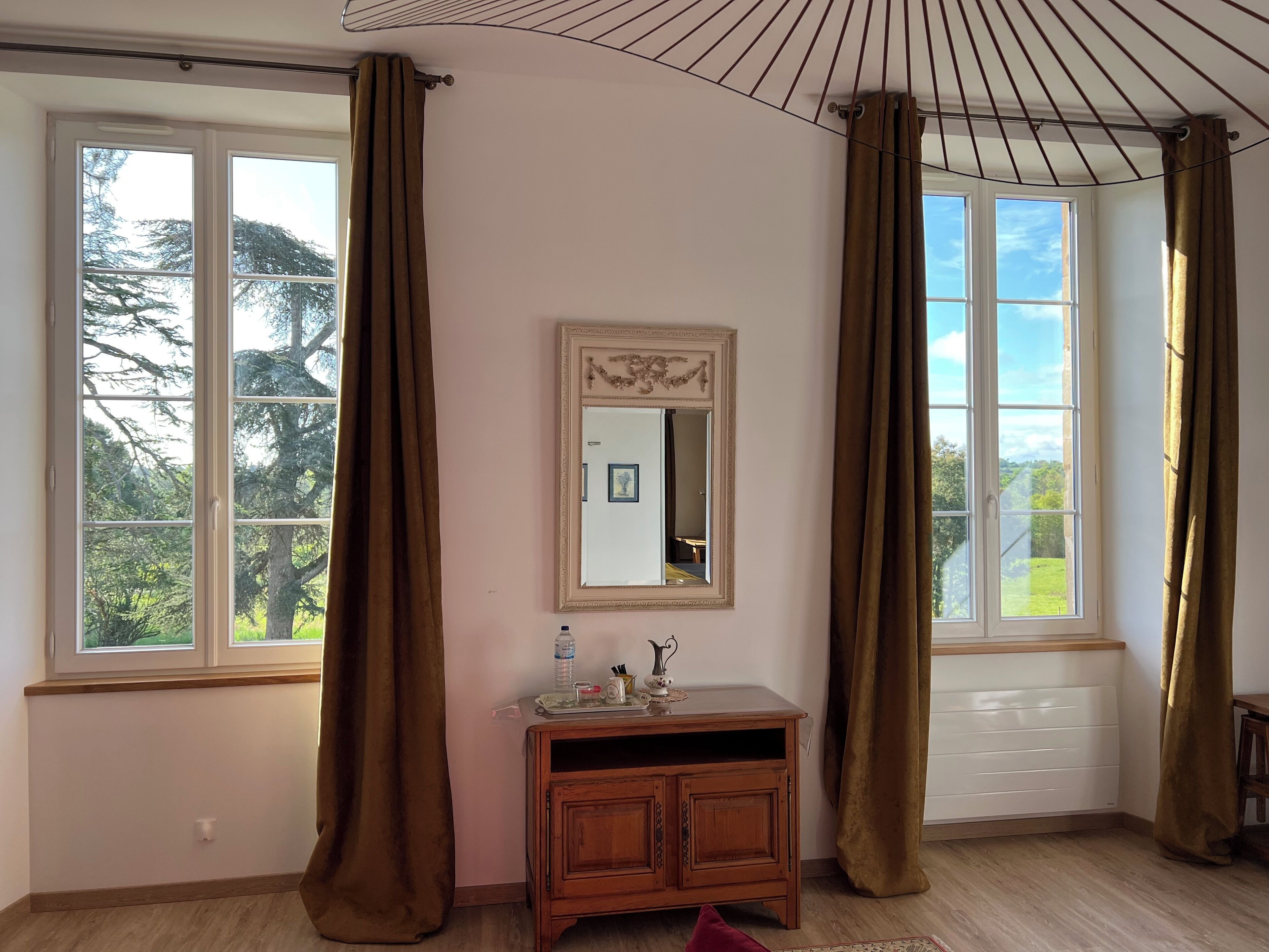 Una habitació amb dues finestres grans, un armari de fusta i un mirall a la paret.