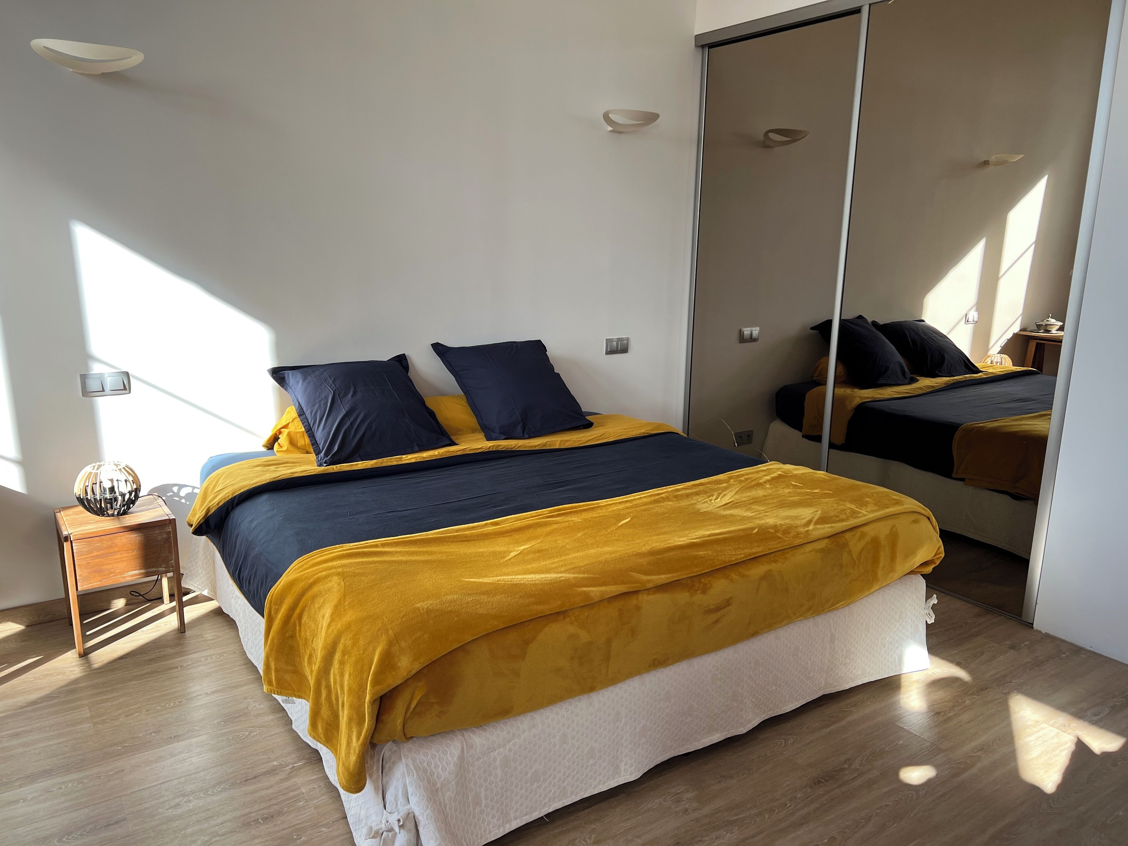 Un dormitorio moderno con cama, mesita de noche y espejo.