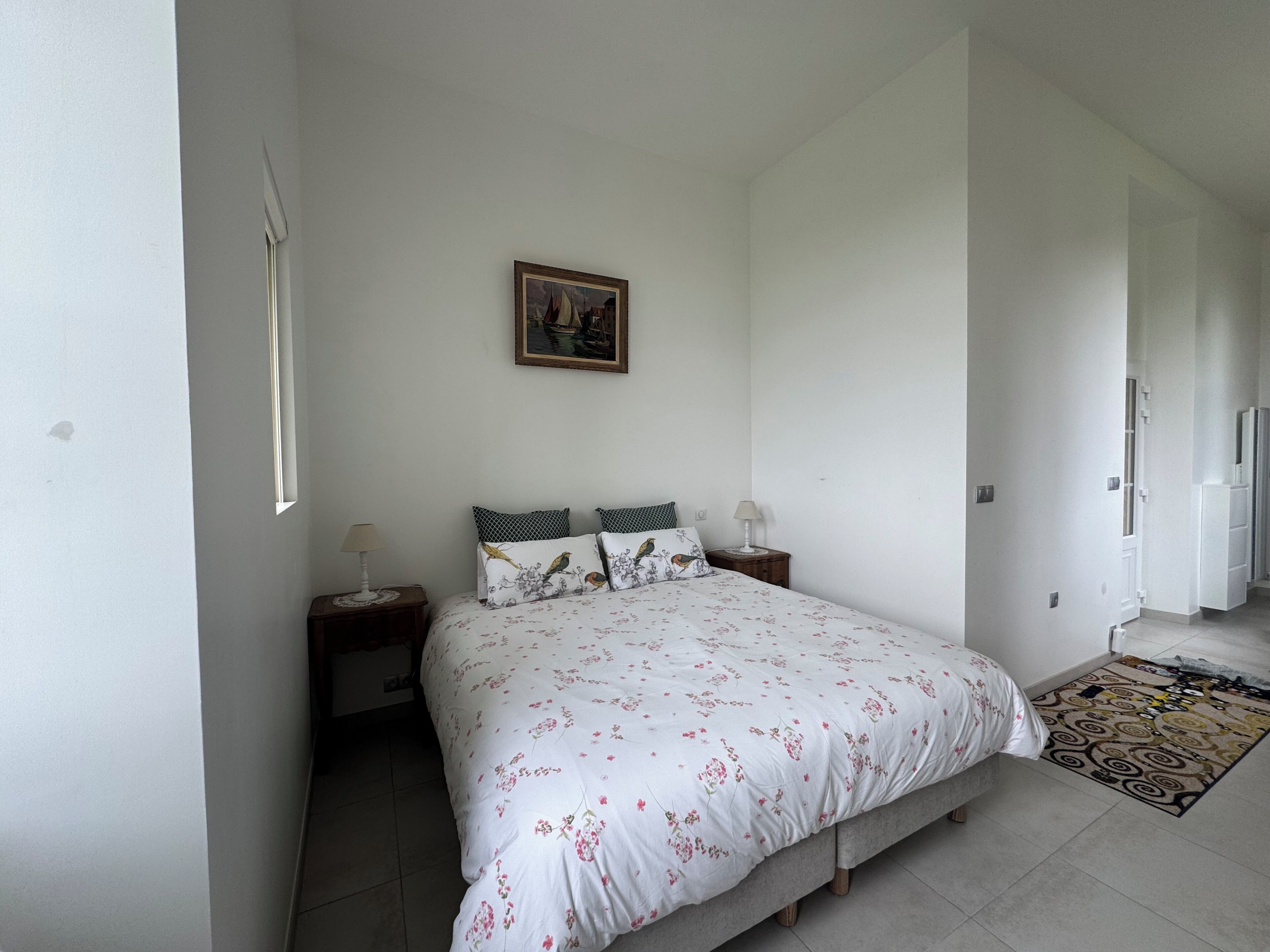 A bedroom with a bed, two nightstands, a lamp, a painting, and a patterned rug.