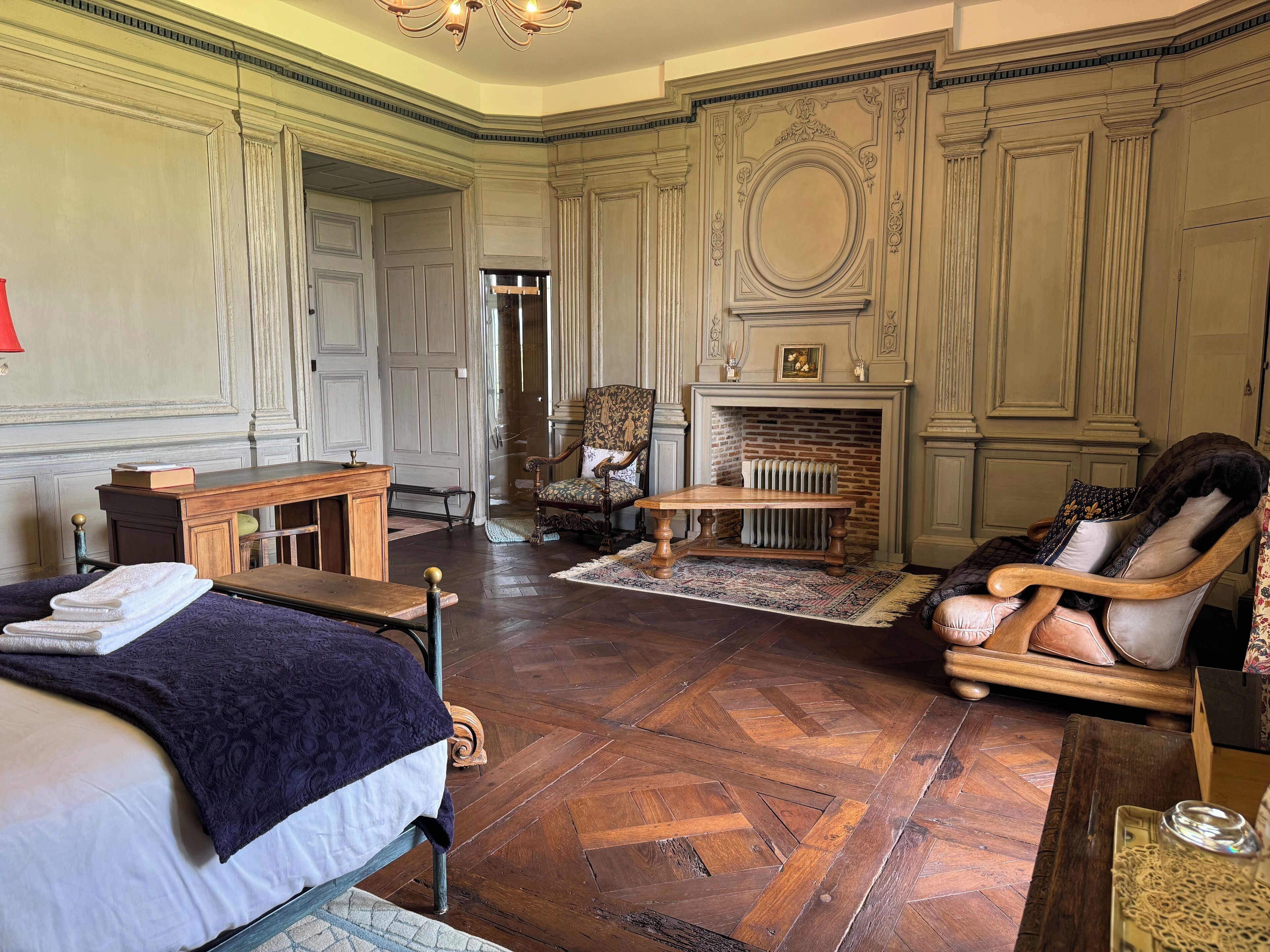 A traditional room with a bed, a wooden table, a chair, and a fireplace.