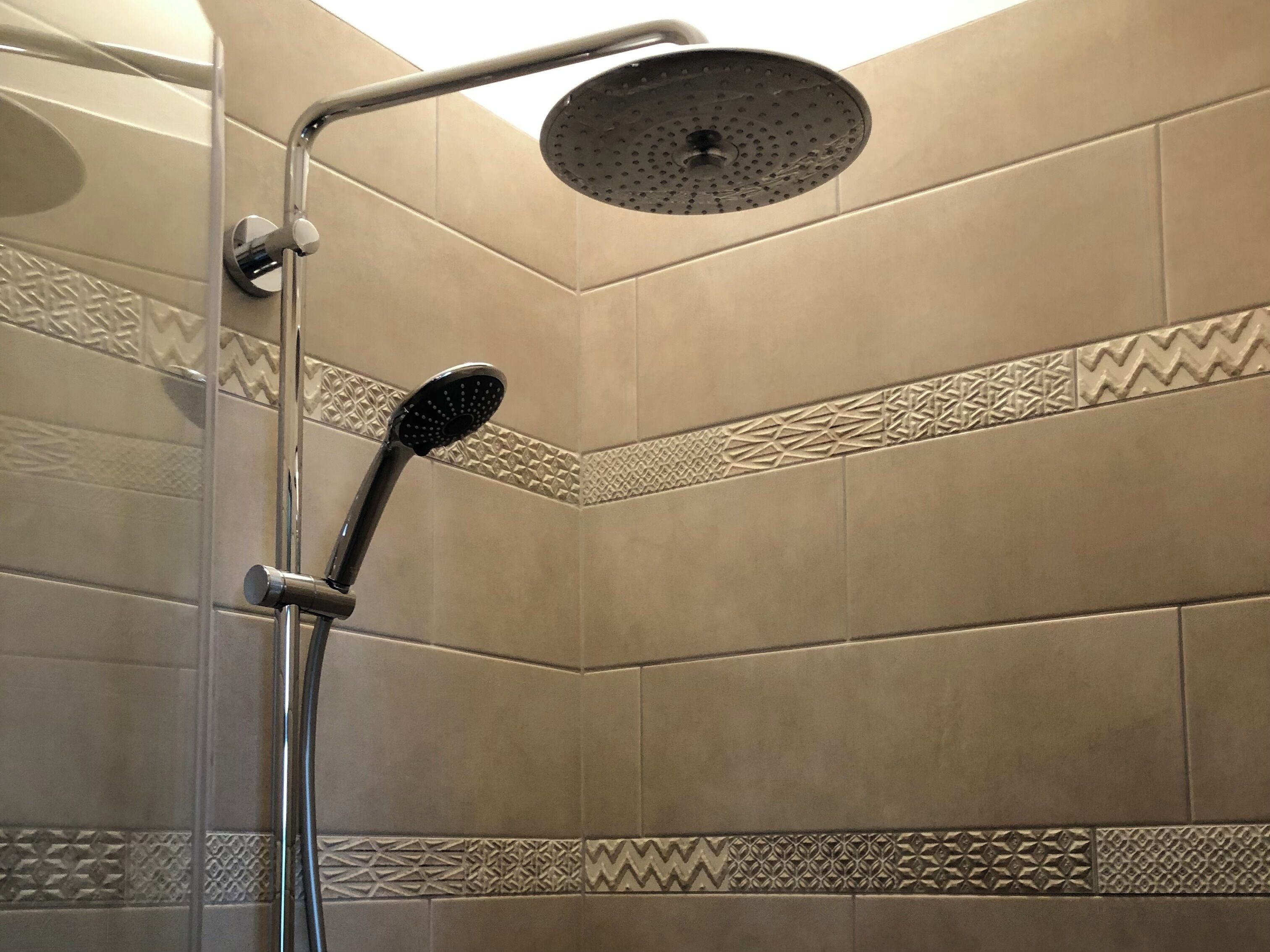 Ducha con cabezal de ducha manual y cabezal de ducha de lluvia empotrado en un baño con azulejos.