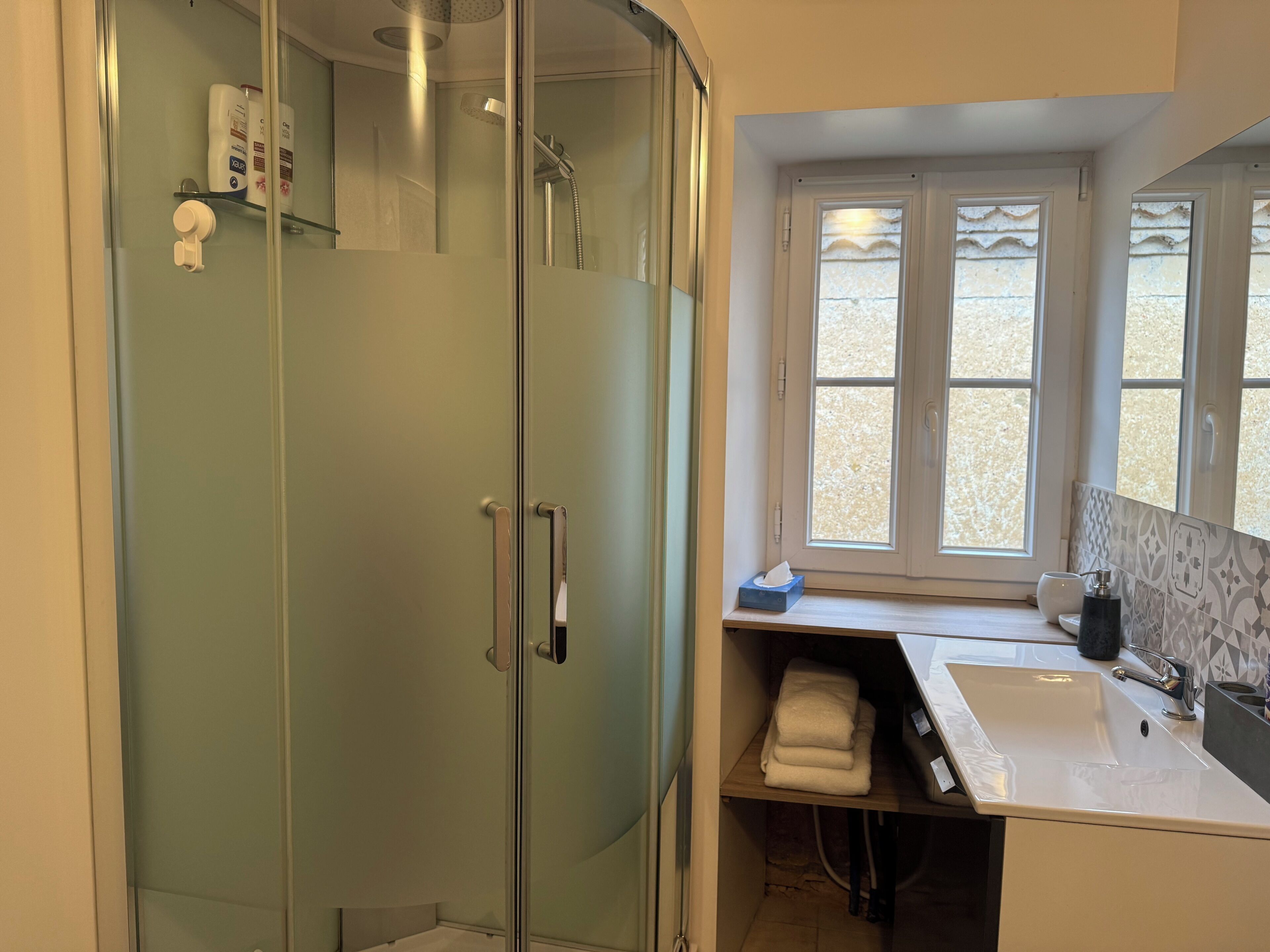 Une salle de bain avec une douche à parois de verre, un lavabo et une fenêtre ornée de carreaux décoratifs.