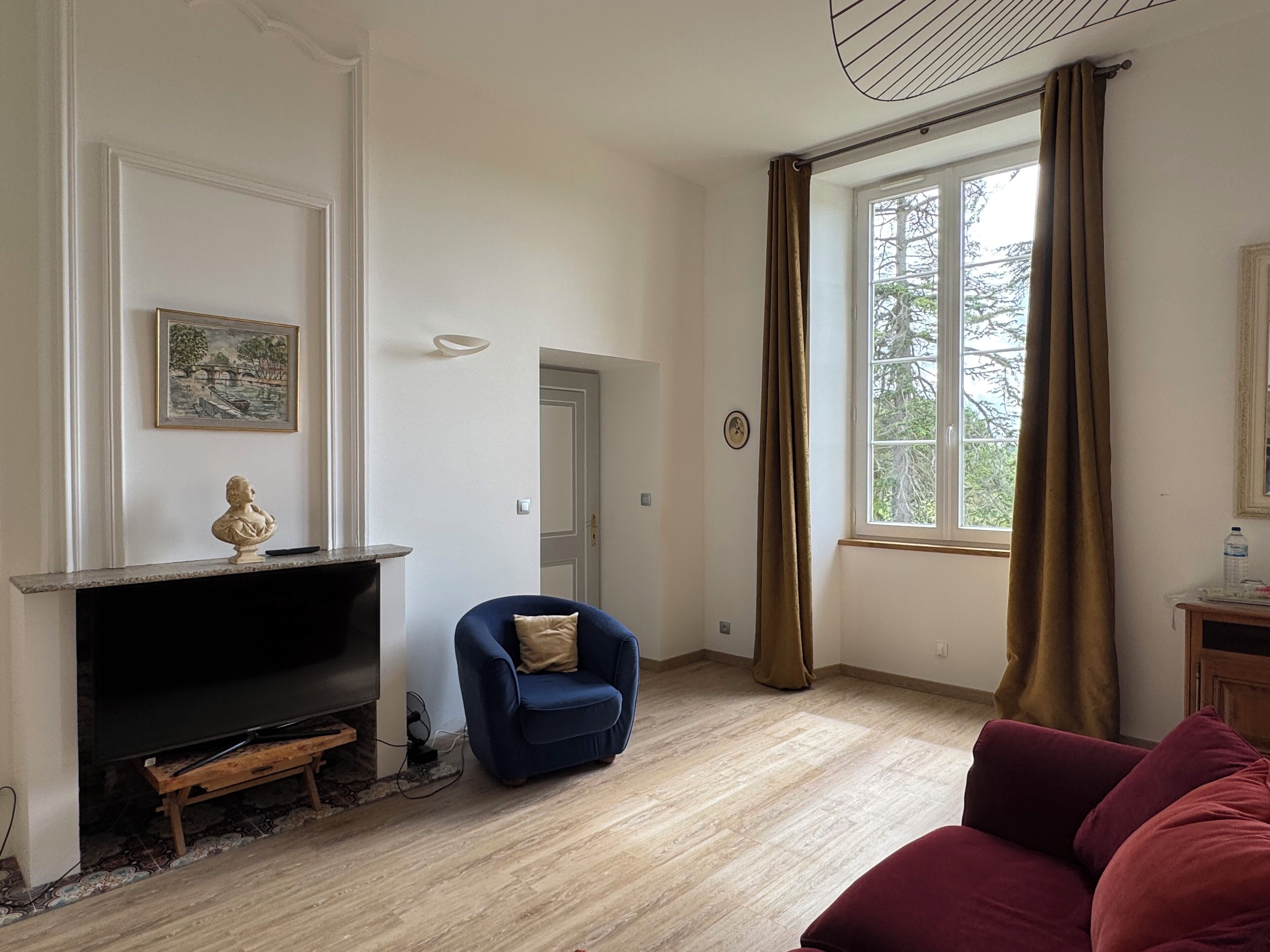 A living room with a fireplace, a blue armchair, a red sofa, and a window with curtains.