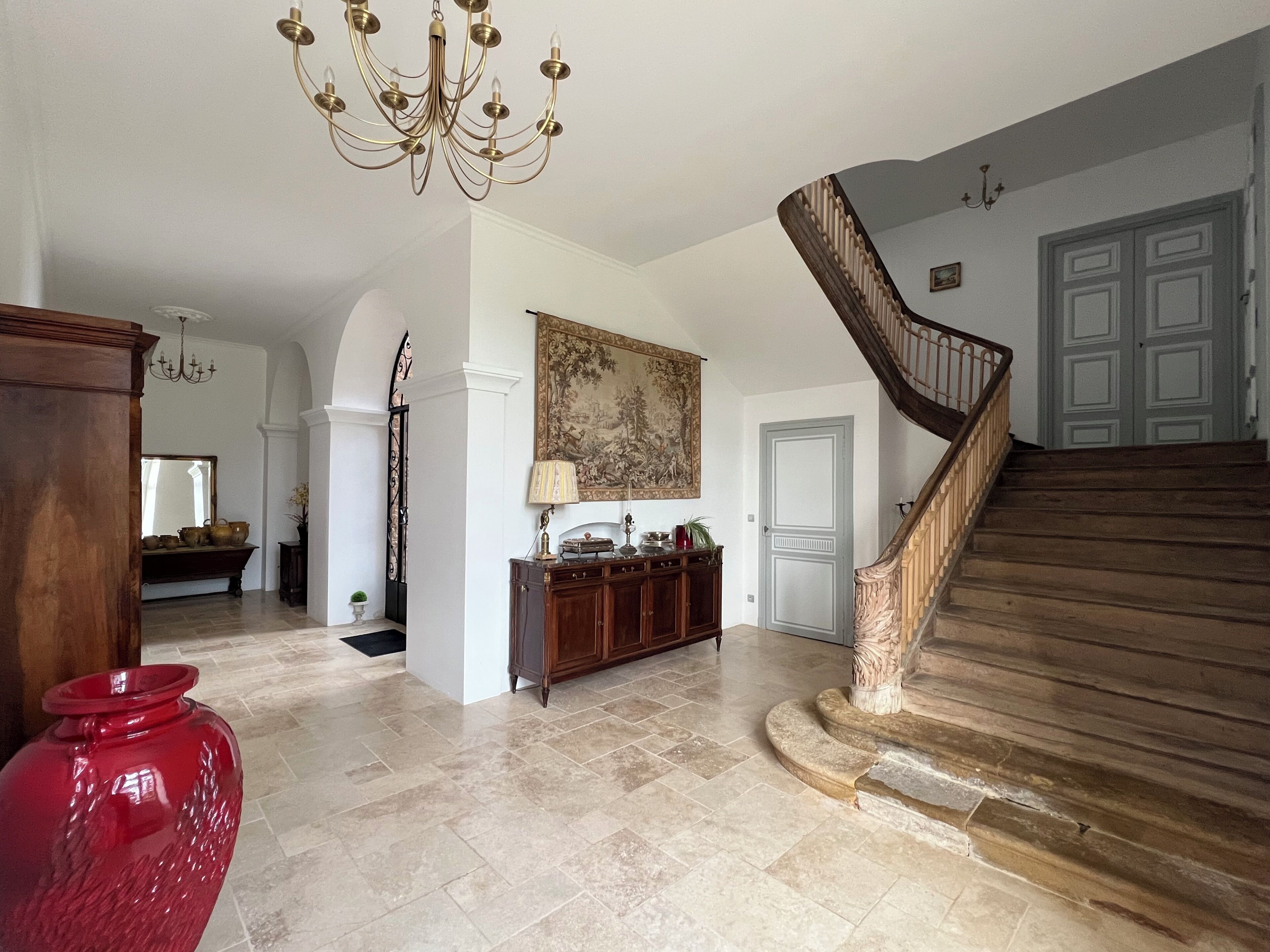 Un vestíbulo espacioso con una escalera imponente, un candelabro y un cuadro grande en la pared.