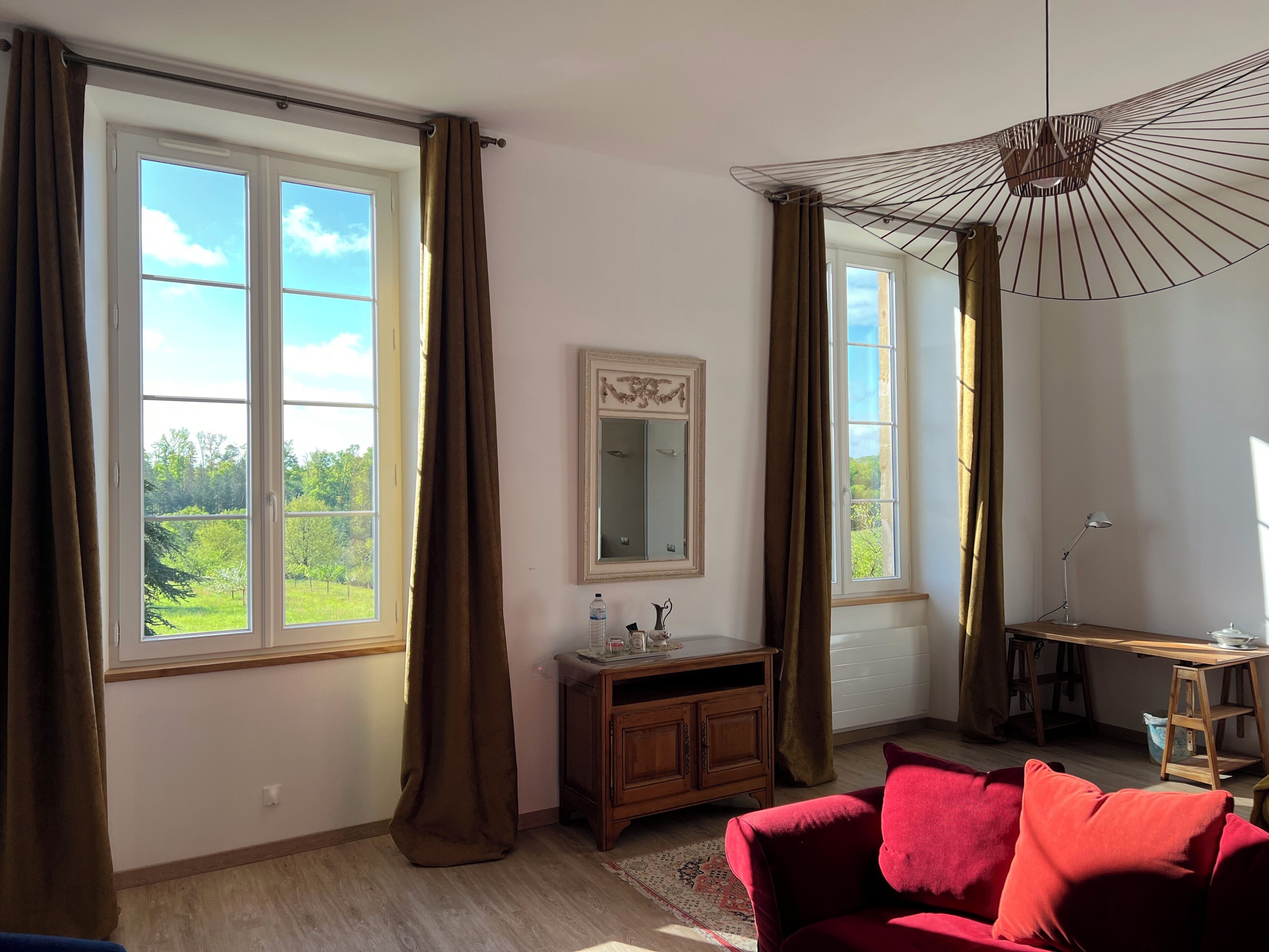 A room with large windows, a wooden cabinet, a red sofa, and a hanging light fixture.