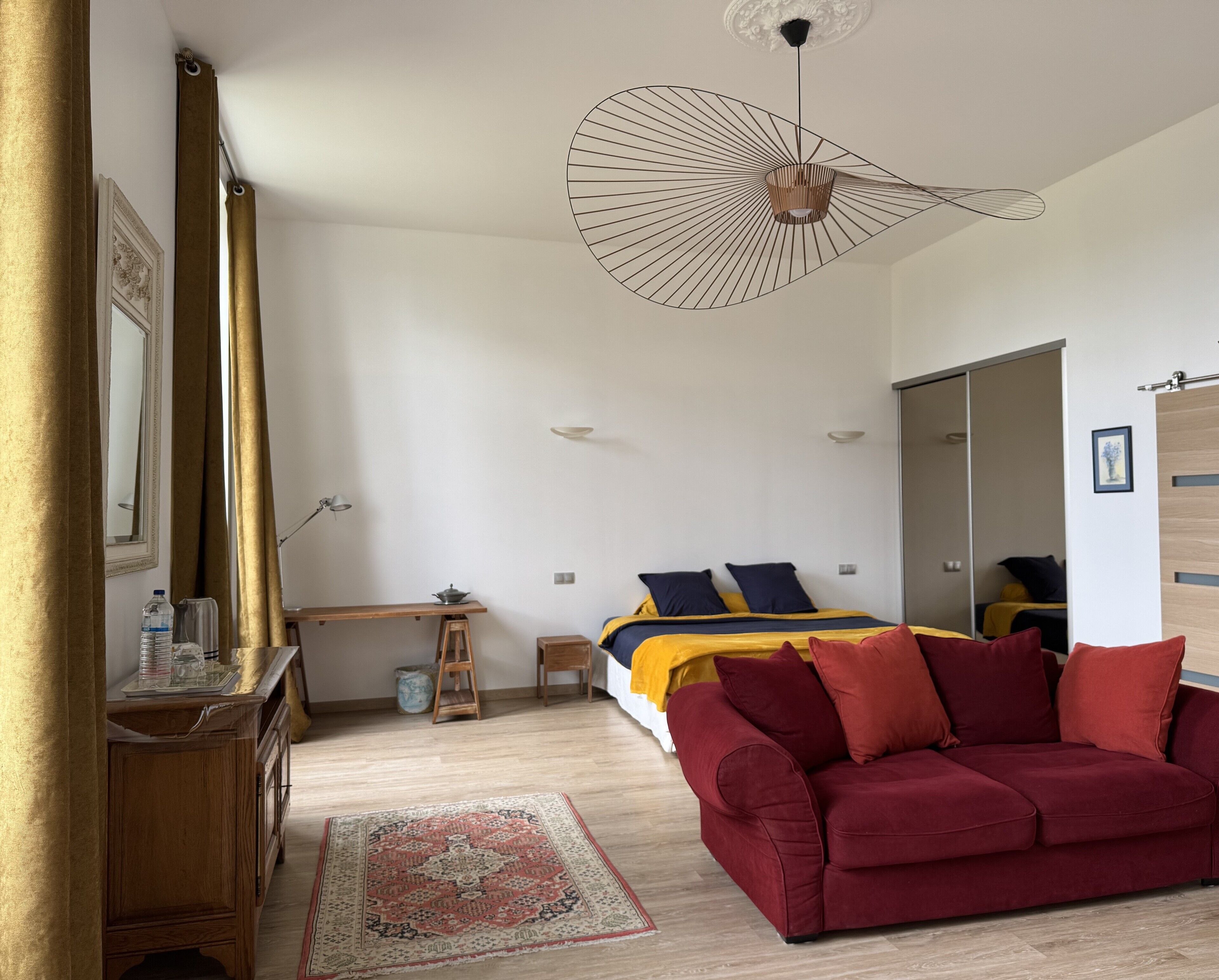 Une chambre à coucher moderne avec un lit en bois, un canapé rouge, une commode en bois et un grand miroir.