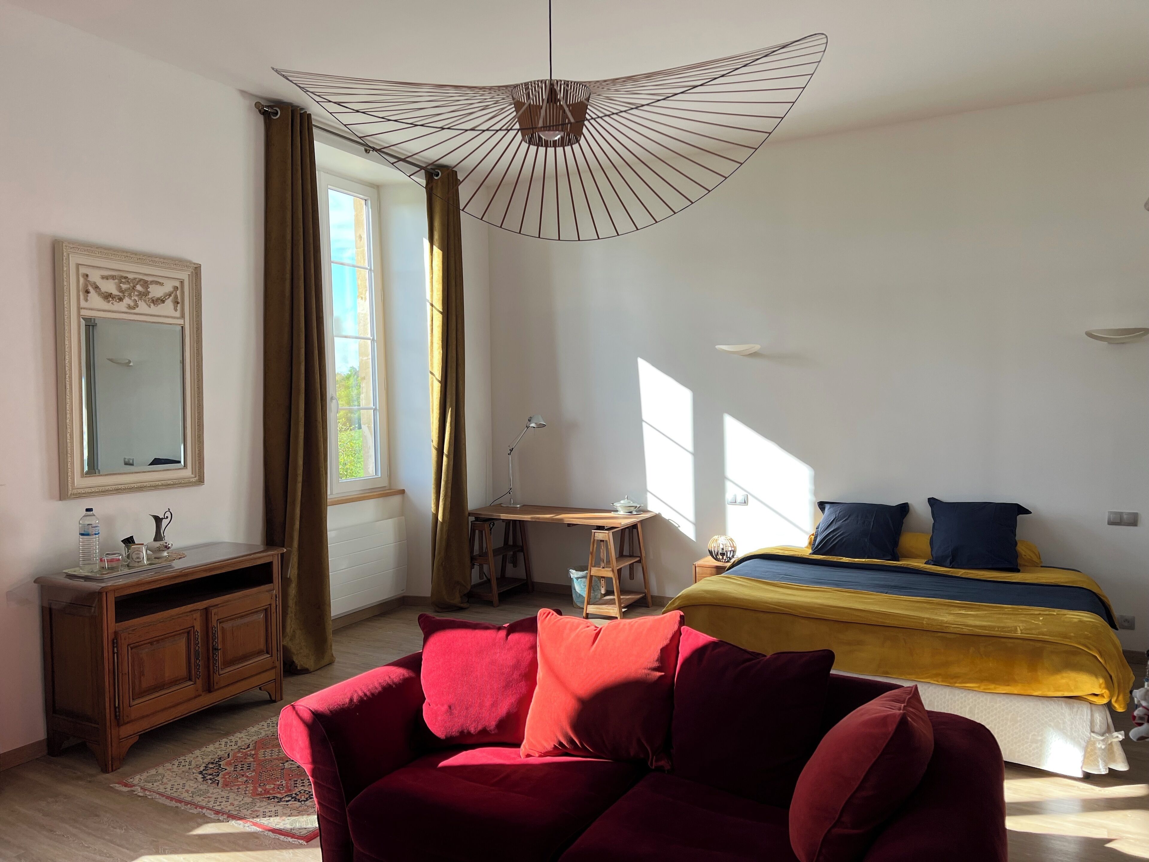 Een slaapkamer met een bed, een bureau, een stoel, een spiegel en een raam met gordijnen.