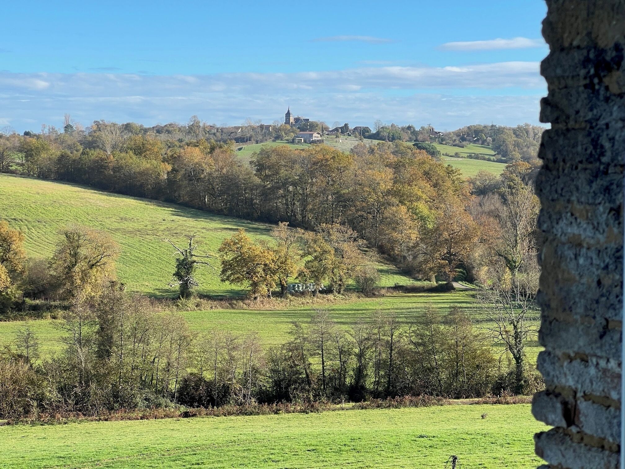 A rural landscape with rolling hills, trees, and a distant building.