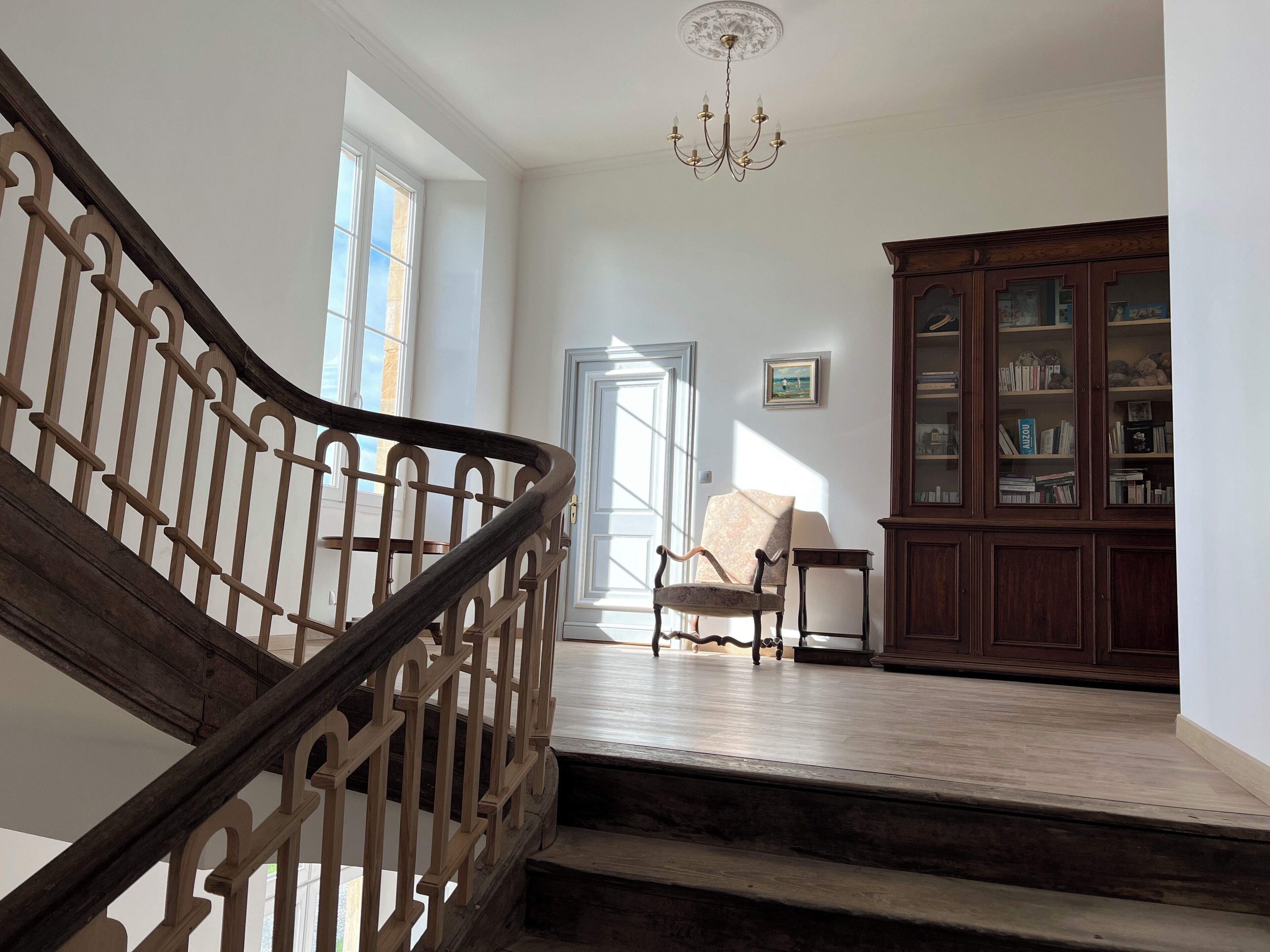 A staircase with a wooden railing leading to a room with a chair, a small table, and a bookcase.