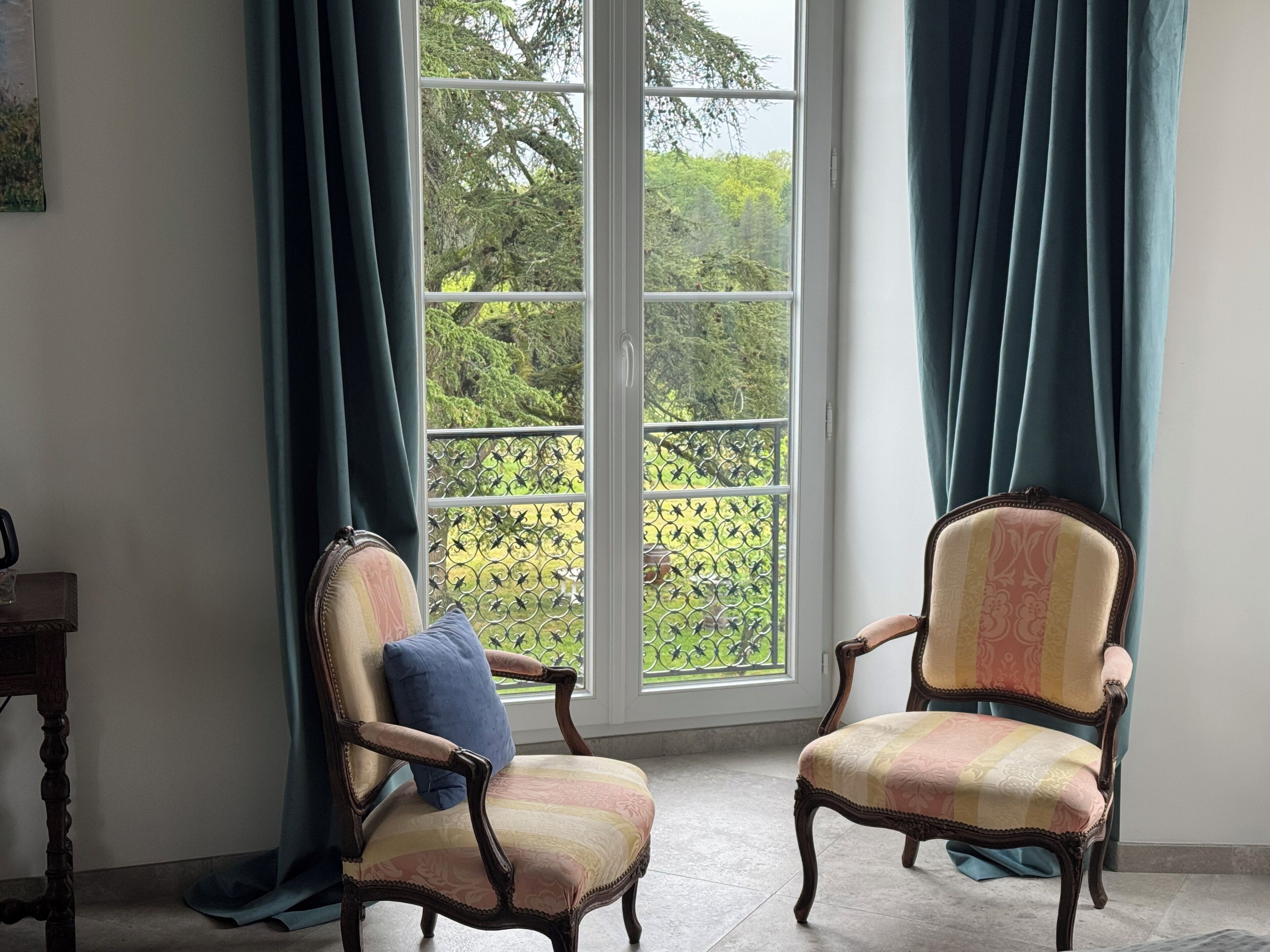 Ein Zimmer mit zwei Polstersesseln, einem großen Fenster mit Blick auf Grünflächen und einem Holztisch.