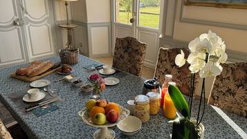 Een ontbijttafel gedekt met fruit, gebak en drankjes, met uitzicht op groen.