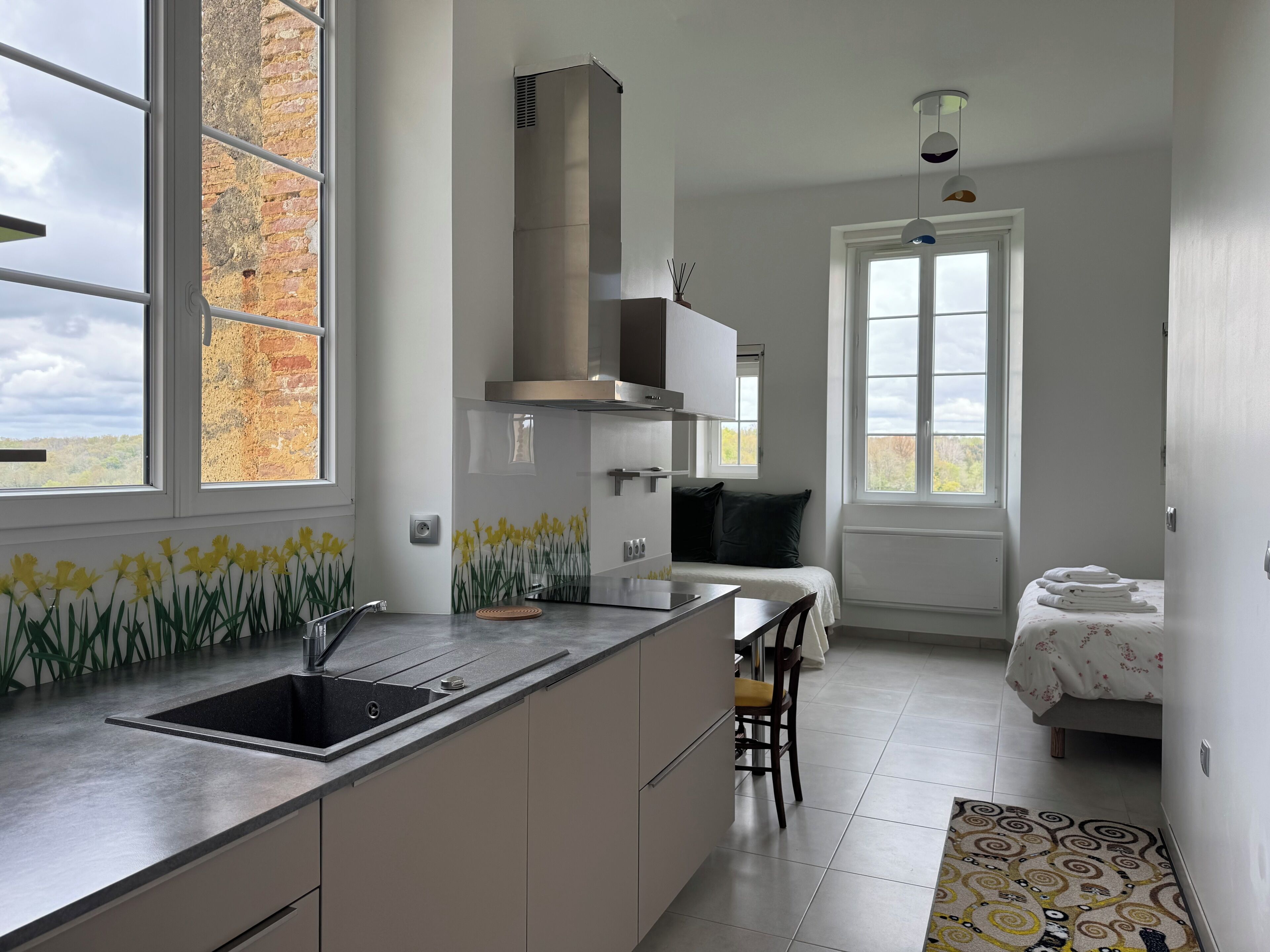 A modern kitchen with a large window, a built-in stove, and a dining area with a chair.