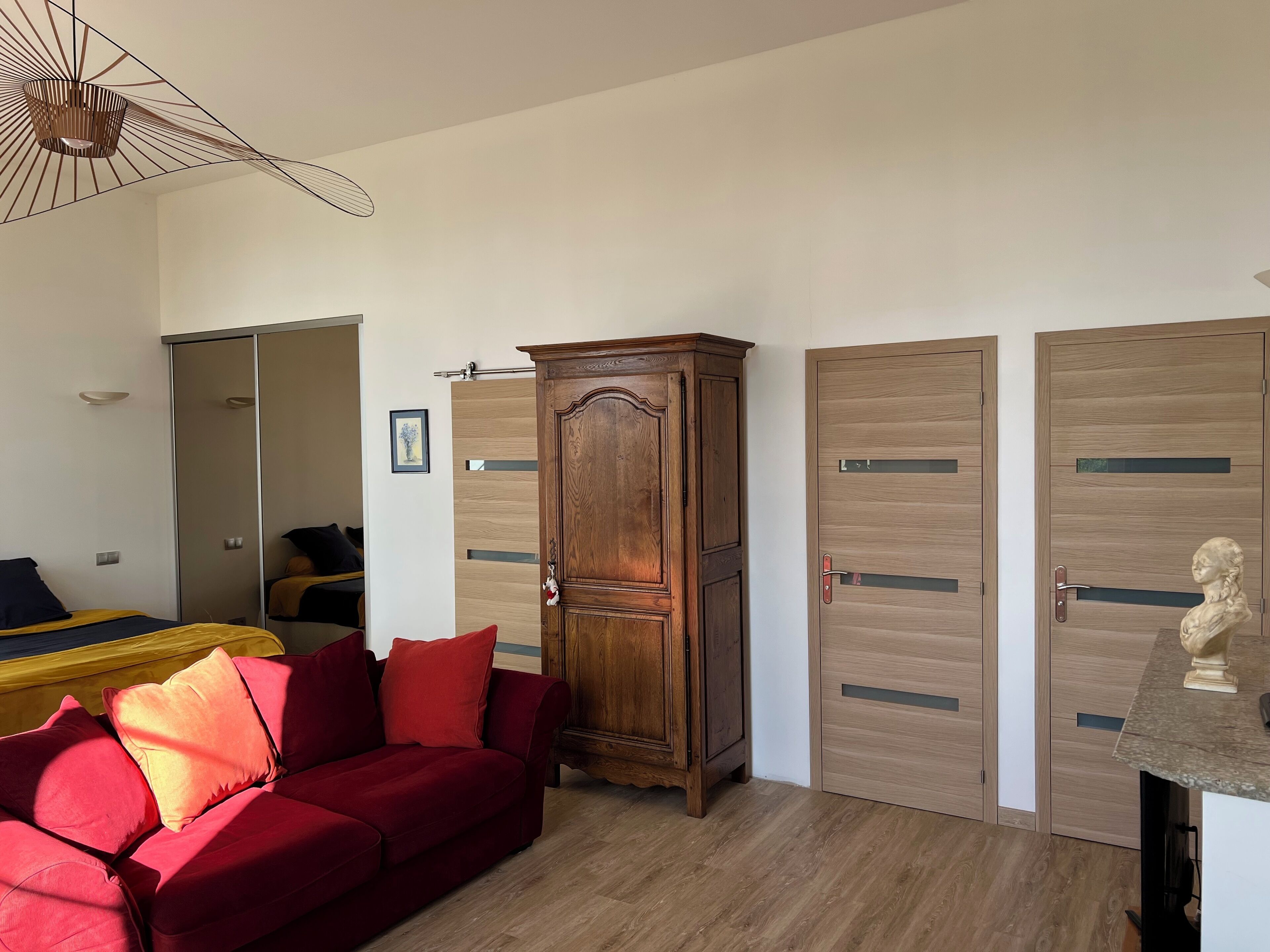 A room with a red sofa, wooden wardrobe, and a mirror.
