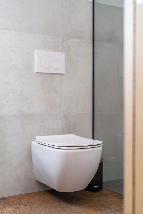 Ein modernes Badezimmer mit Toilette in Weiß, einer Duschkabine aus Glas und einer an der Wand montierten Bedienkonsole.