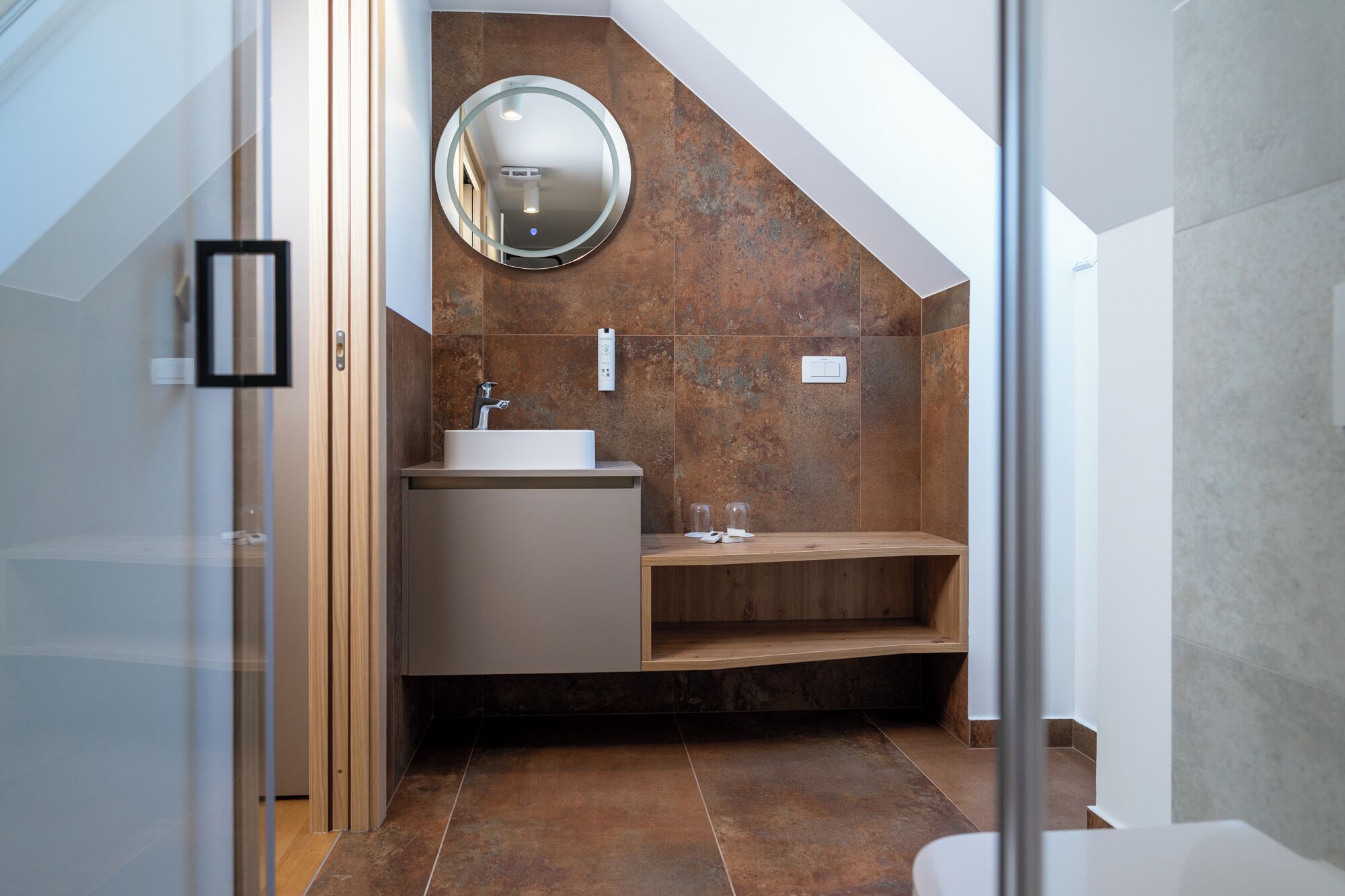 Un baño moderno con tocador de madera, un espejo redondo y un lavabo empotrado.