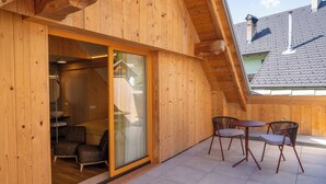 A wooden cabin with a glass door leading to a bathroom, a small patio with two chairs and a table, and a sloped roof. - Landhouse Bled (Bled)