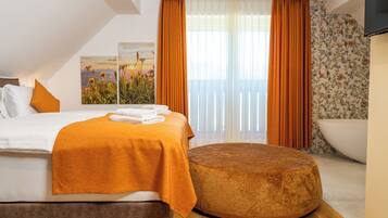 A modern hotel room with a bed, a round ottoman, a large window with curtains, and a view of the sea.