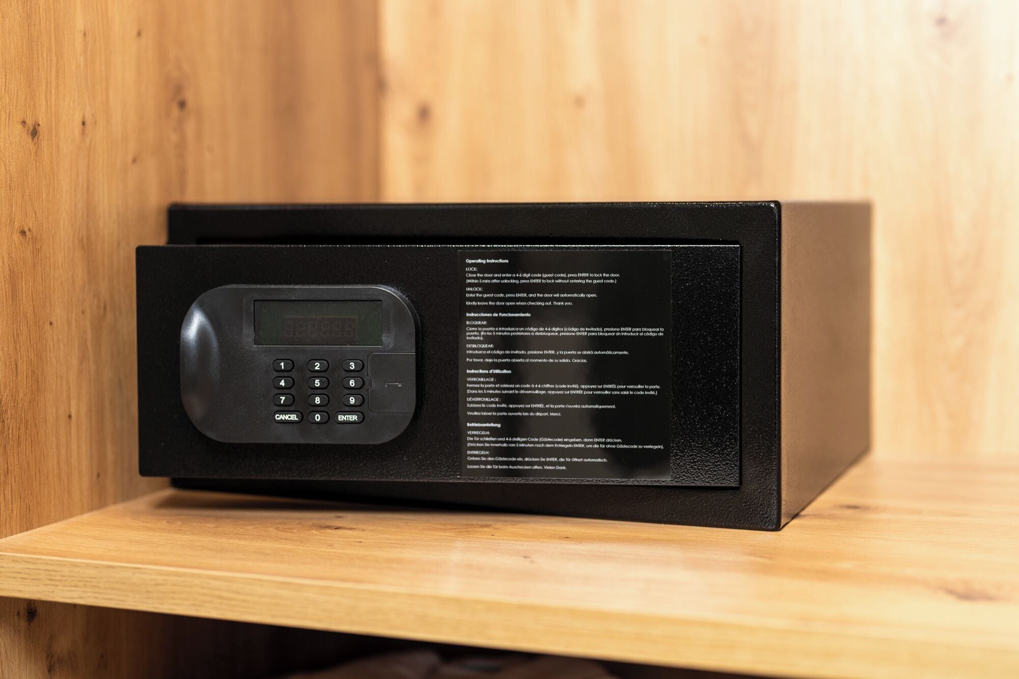 A black electronic device with a keypad and a display screen, placed on a wooden shelf.