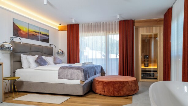 A modern bedroom with a large bed, a round ottoman, a bathtub, and a view of the outdoors. - Landhouse Bled (Bled)