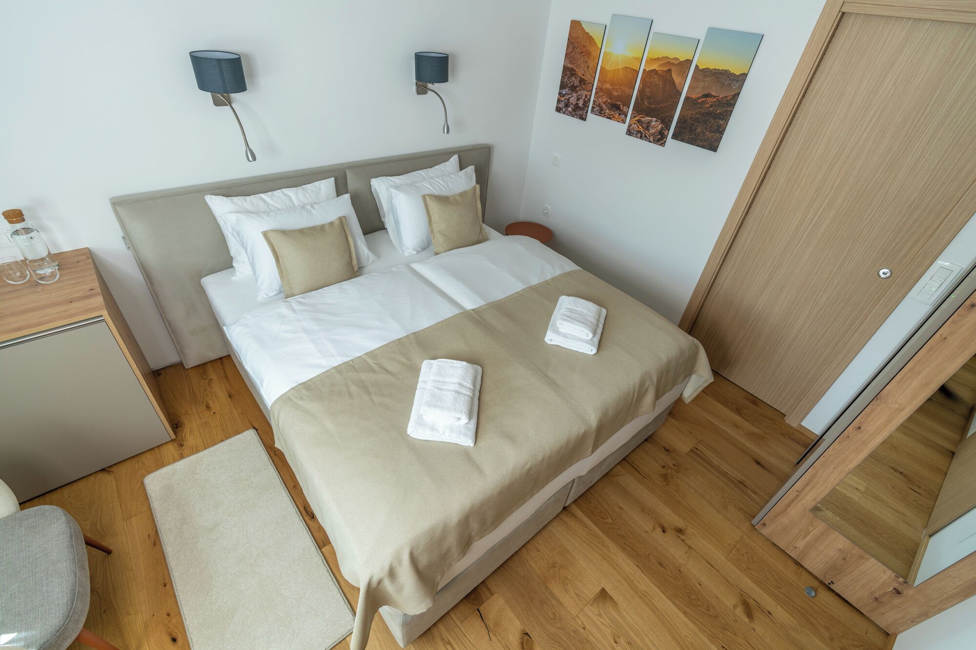 A neatly arranged hotel room with a bed, bedside tables, a desk, and a wardrobe.