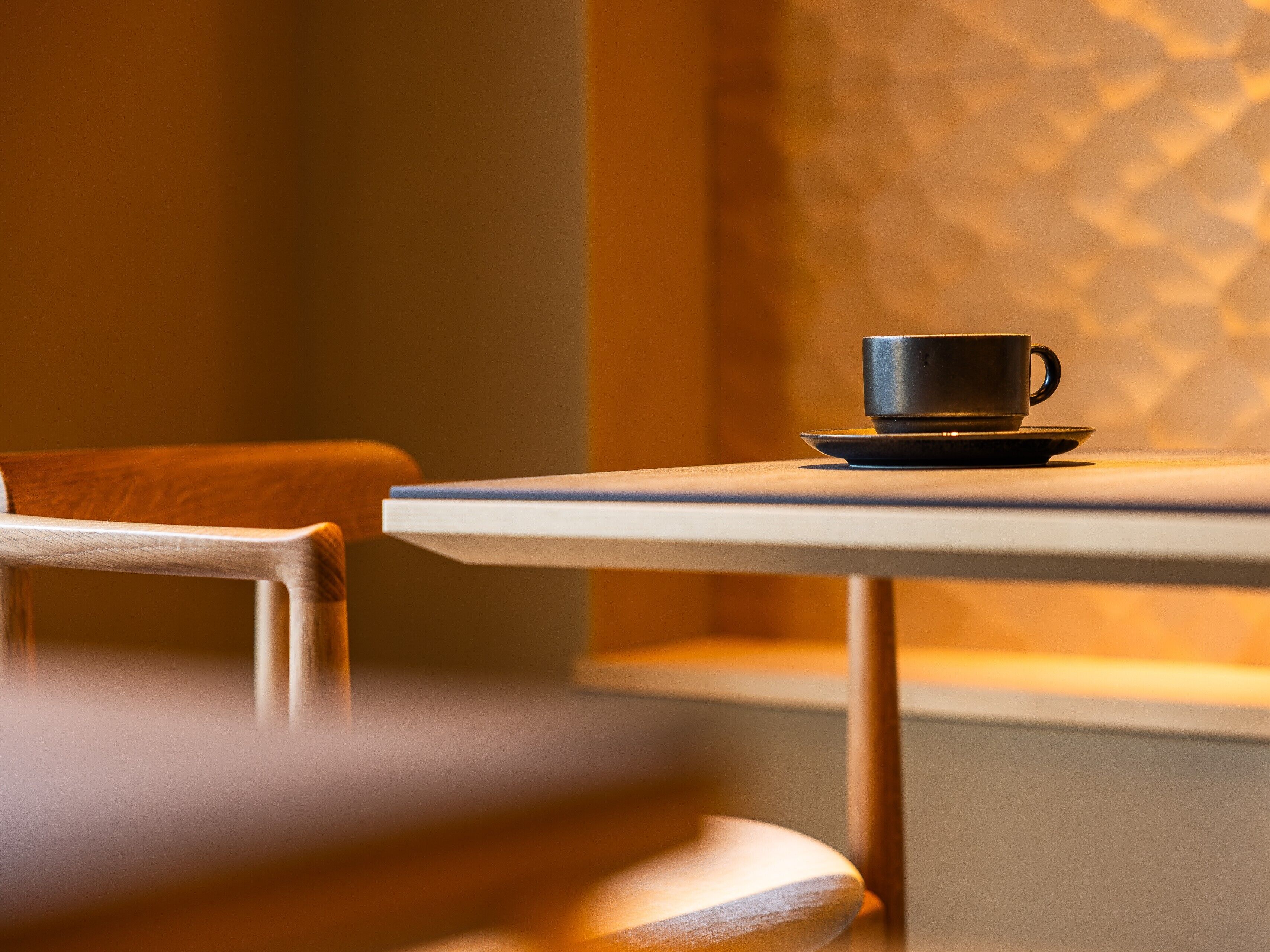 Un tavolo con tazza e piattino, una sedia e una parete strutturata sullo sfondo.