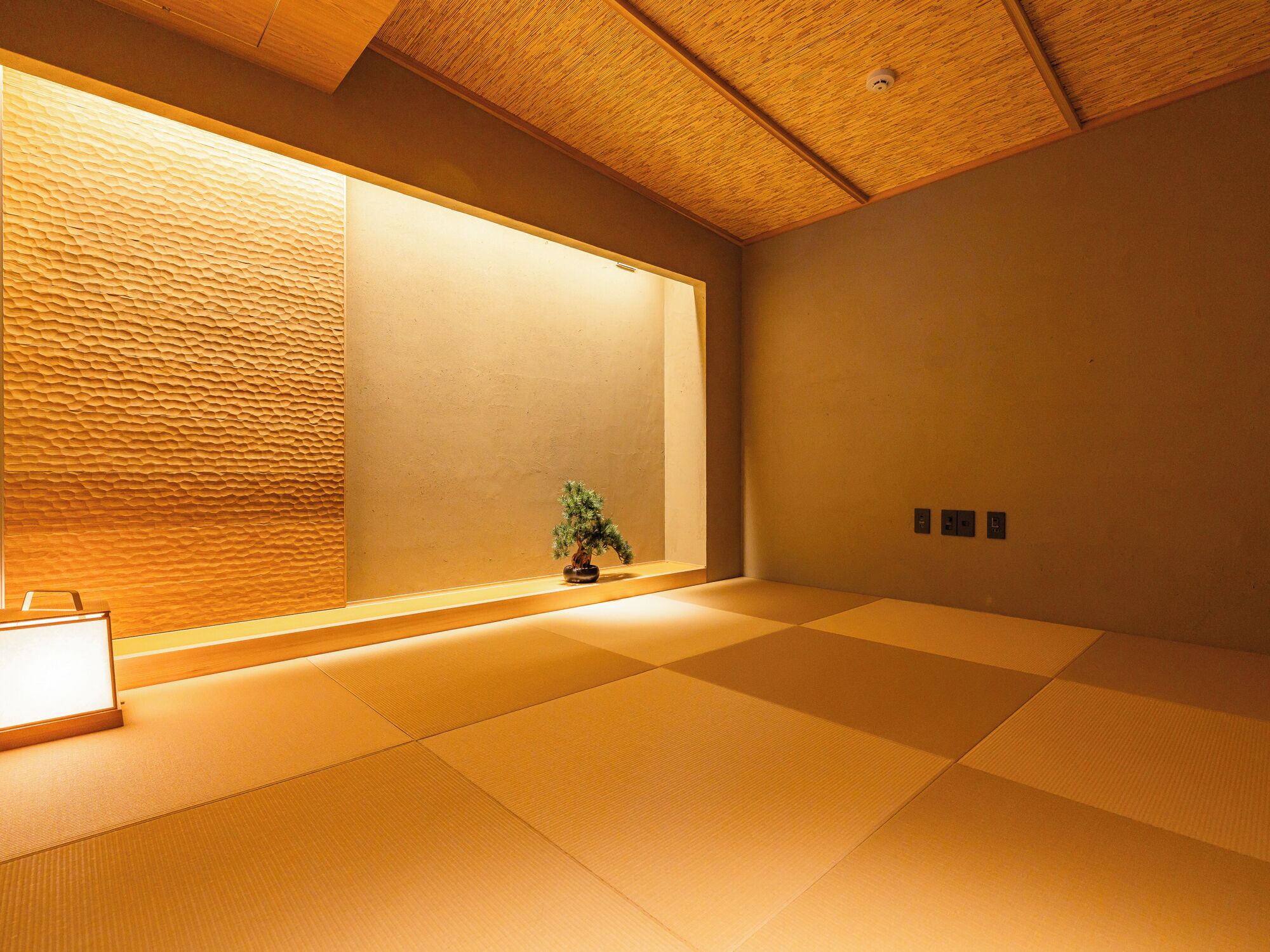 A tatami mat room with a shoji screen, a small bonsai tree, and a traditional Japanese-style lamp.