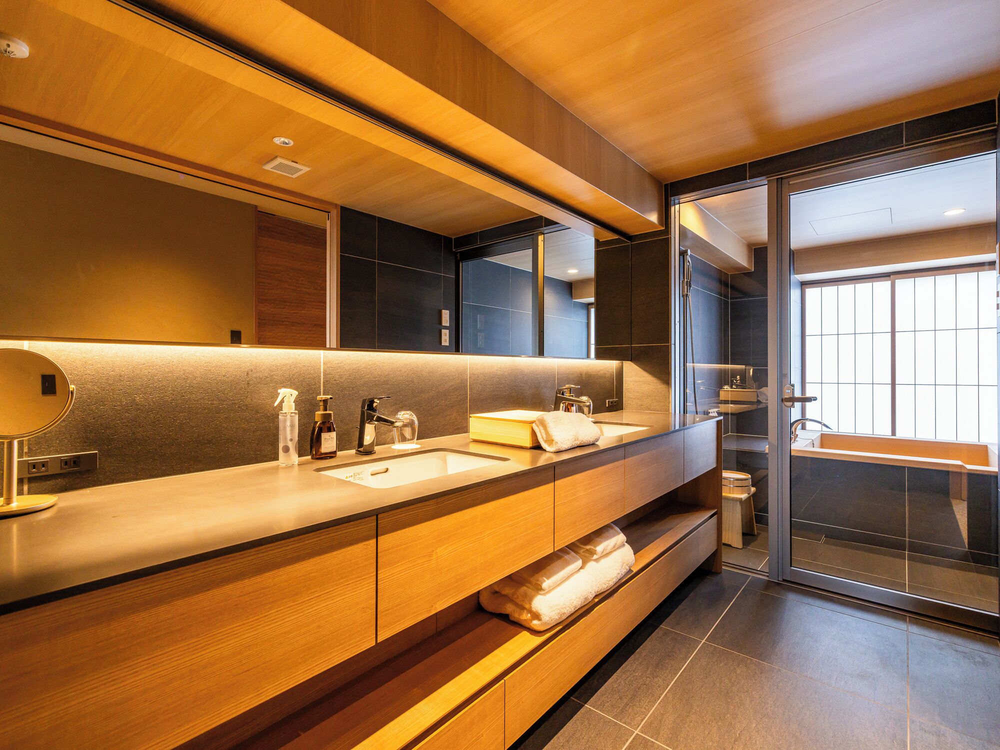 A modern bathroom with a wooden vanity, two sinks, a large mirror, and a glass shower enclosure.