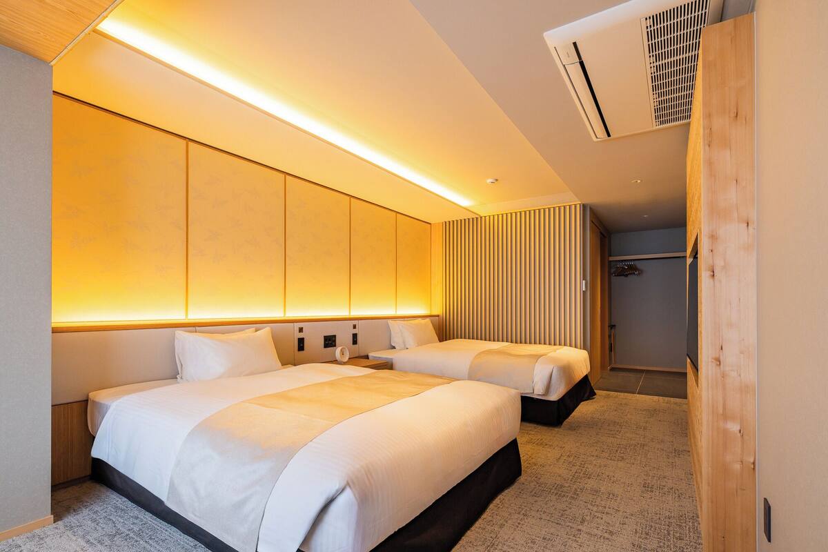 Une chambre d’hôtel moderne avec deux lits, une armoire en bois et un espace douche.