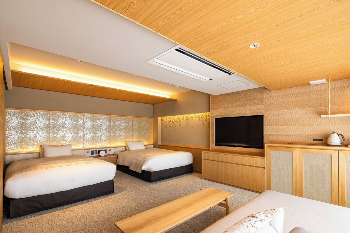 Une chambre d’hôtel moderne équipée de deux lits, d’un téléviseur à écran plat, d’un banc en bois et d’une petite kitchenette.
