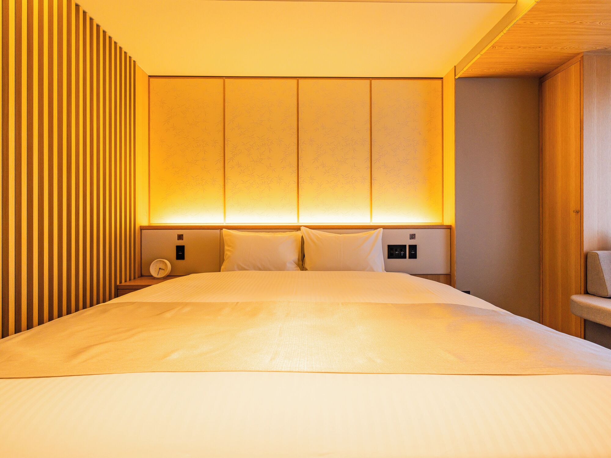 Een moderne hotelkamer met een groot bed, houten lambrisering aan een muur en warme sfeerverlichting.