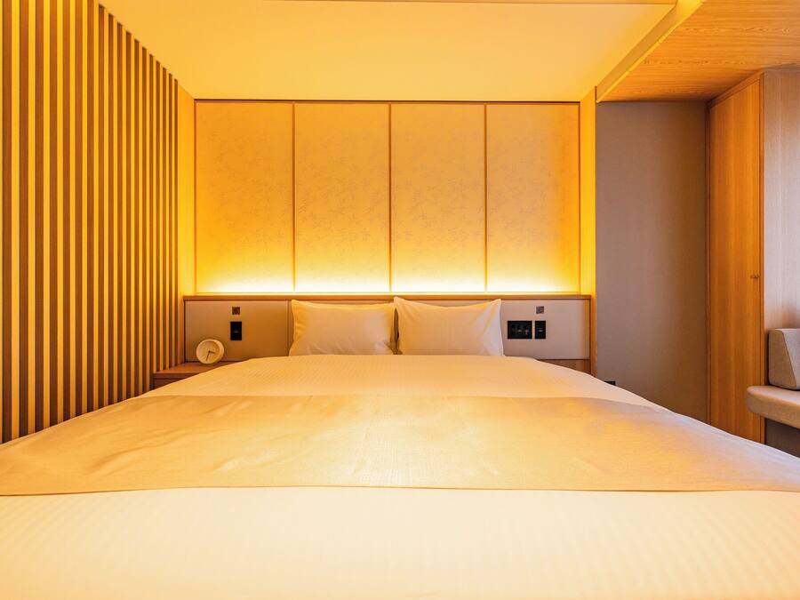 Een moderne hotelkamer met een groot bed, houten lambrisering aan een muur en warme sfeerverlichting.