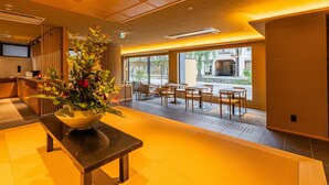 Un hall d’hôtel moderne doté d’un comptoir d’accueil, d’un espace salon et de grandes fenêtres offrant une vue sur l’extérieur.